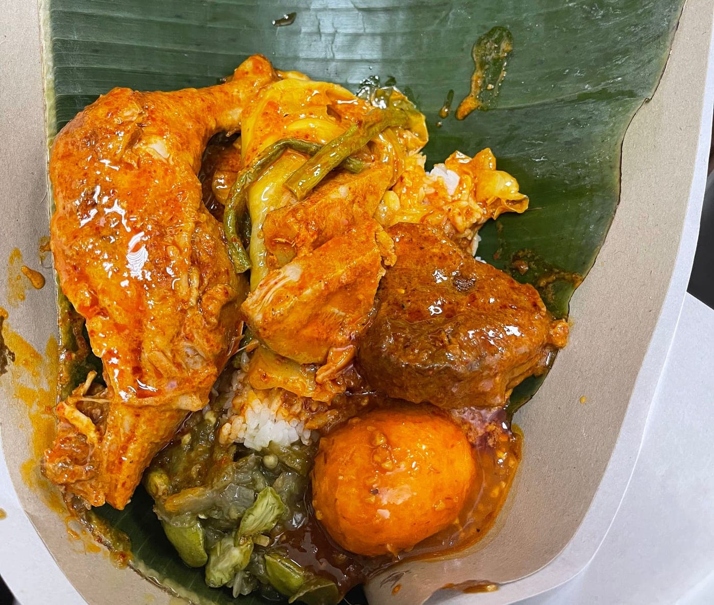 Nasi Padang Complete, wrapped in banana leaf: white rice with chicken curry, beef rendang, spicy boiled egg, green chili with stinky bean, and vegetables