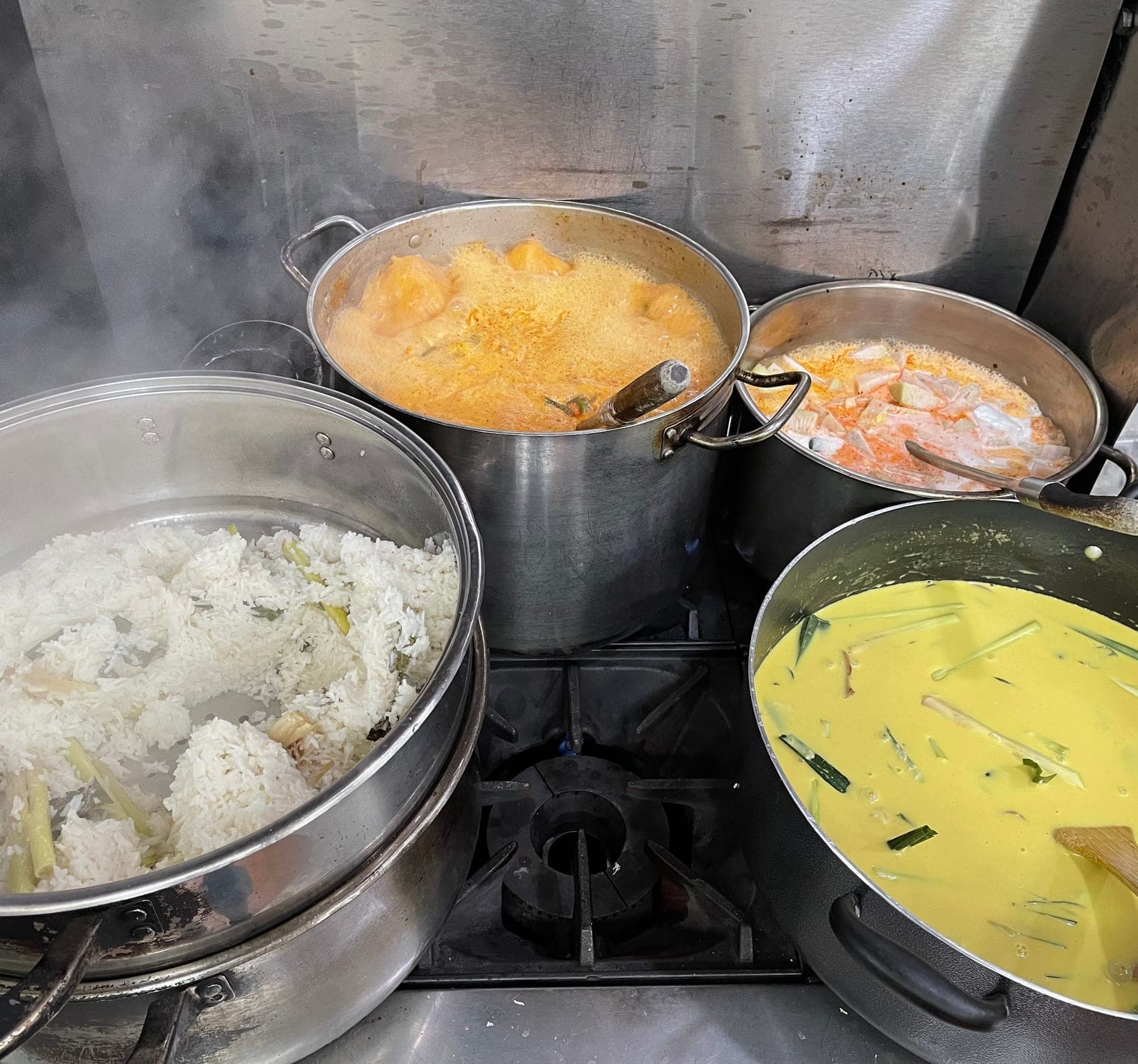 Four pots on the range: a steamer of Nasi Uduk, Sayur Lodeh, Sayur Nangka, and a wide wok of Nasi Kuning part-cooked with lemongrass and pandan