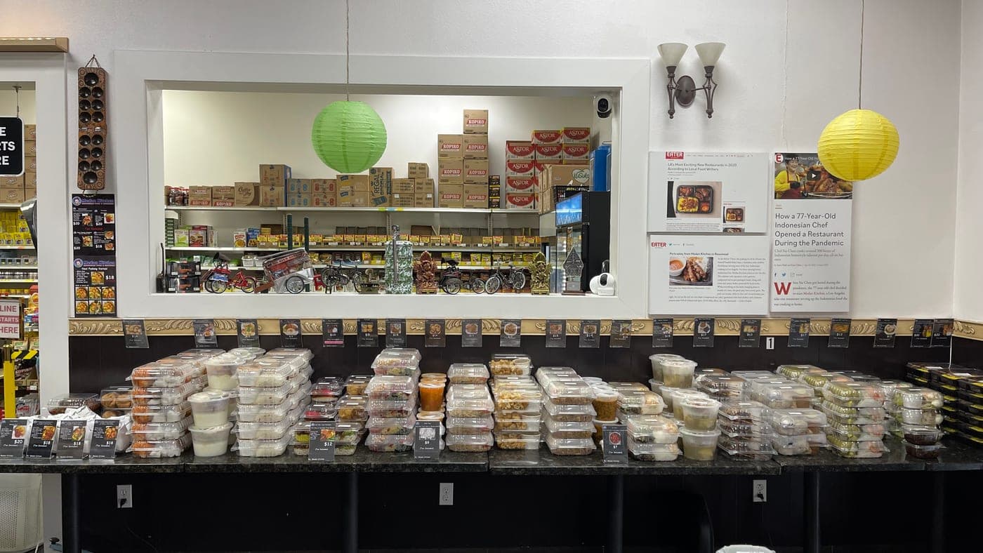 The left-hand counter stacked with packed containers under price tags, the grocery shelves visible through a window behind